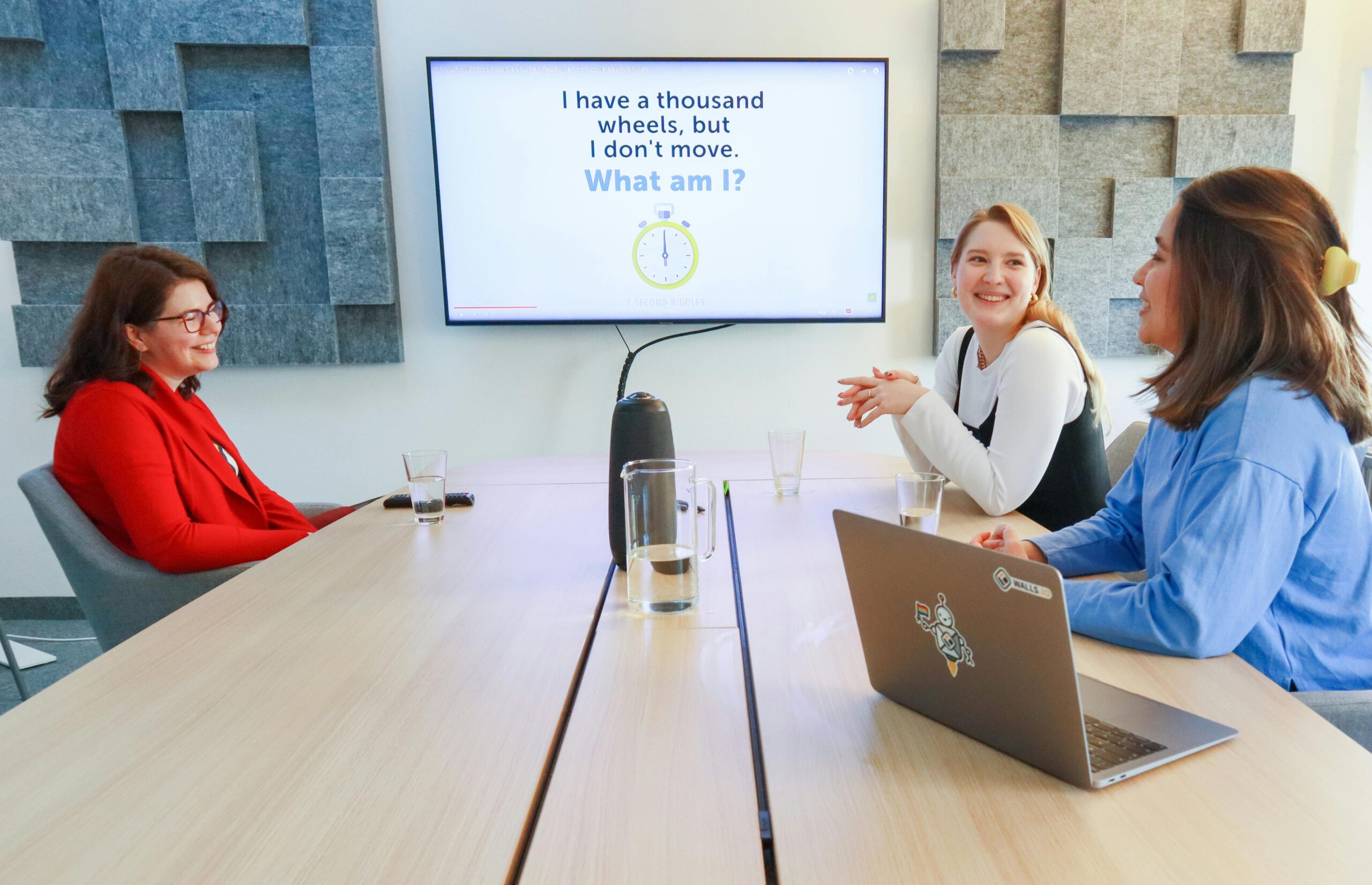 Three women having a discussion in a modern office with a presentation on screen.